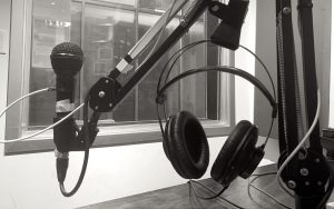 This image shows a close up of a microphone and headphones on a boom arm stand above a wooden desk, with a window in the background