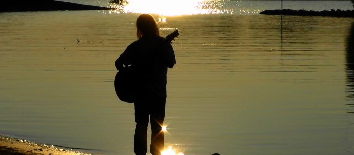 person with guitar in front of river