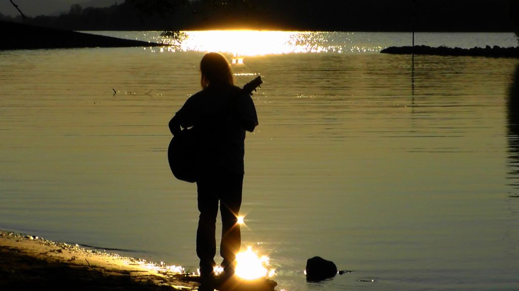 person with guitar in front of river